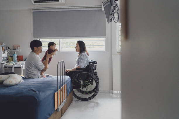 A father holds his infant child up beside his wife who sits in a wheelchair